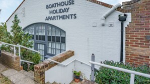 Un edificio con el rótulo "Boathouse Holiday Apartments", fachada blanca, un gran ventanal arqueado y base de ladrillo.