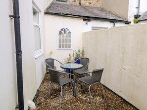A small patio with a round table and four wicker chairs, surrounded by pebbles. - Driftwood Apartment (Morpeth)
