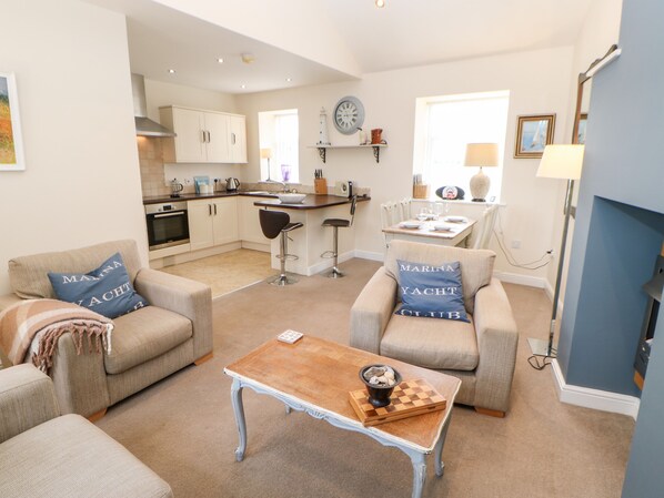 A spacious living area with two armchairs, a coffee table, and a kitchen in the background. - Driftwood Apartment (Morpeth)