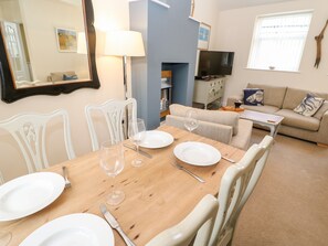 A dining area with a wooden table set for four, white chairs, and a television in the background. - Driftwood Apartment (Morpeth)