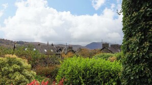 A traditional stone house with a thatched roof, surrounded by lush greenery and a mountainous backdrop. - Walker's Retreat (Ambleside)