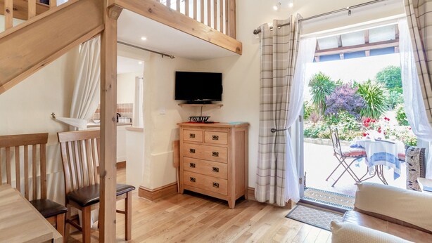 A spacious living area with a wooden staircase, a TV on a wooden cabinet, and a dining area with a table and chairs. - Norbank Cottage (Diss)