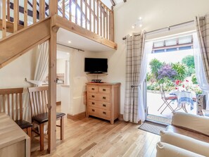 A spacious living area with a wooden staircase, a TV on a wooden cabinet, and a dining area with a table and chairs. - Norbank Cottage (Diss)