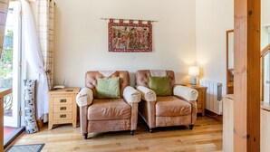 A cozy room with two leather armchairs, a wooden cabinet, a radiator, and a wall tapestry. - Norbank Cottage (Diss)