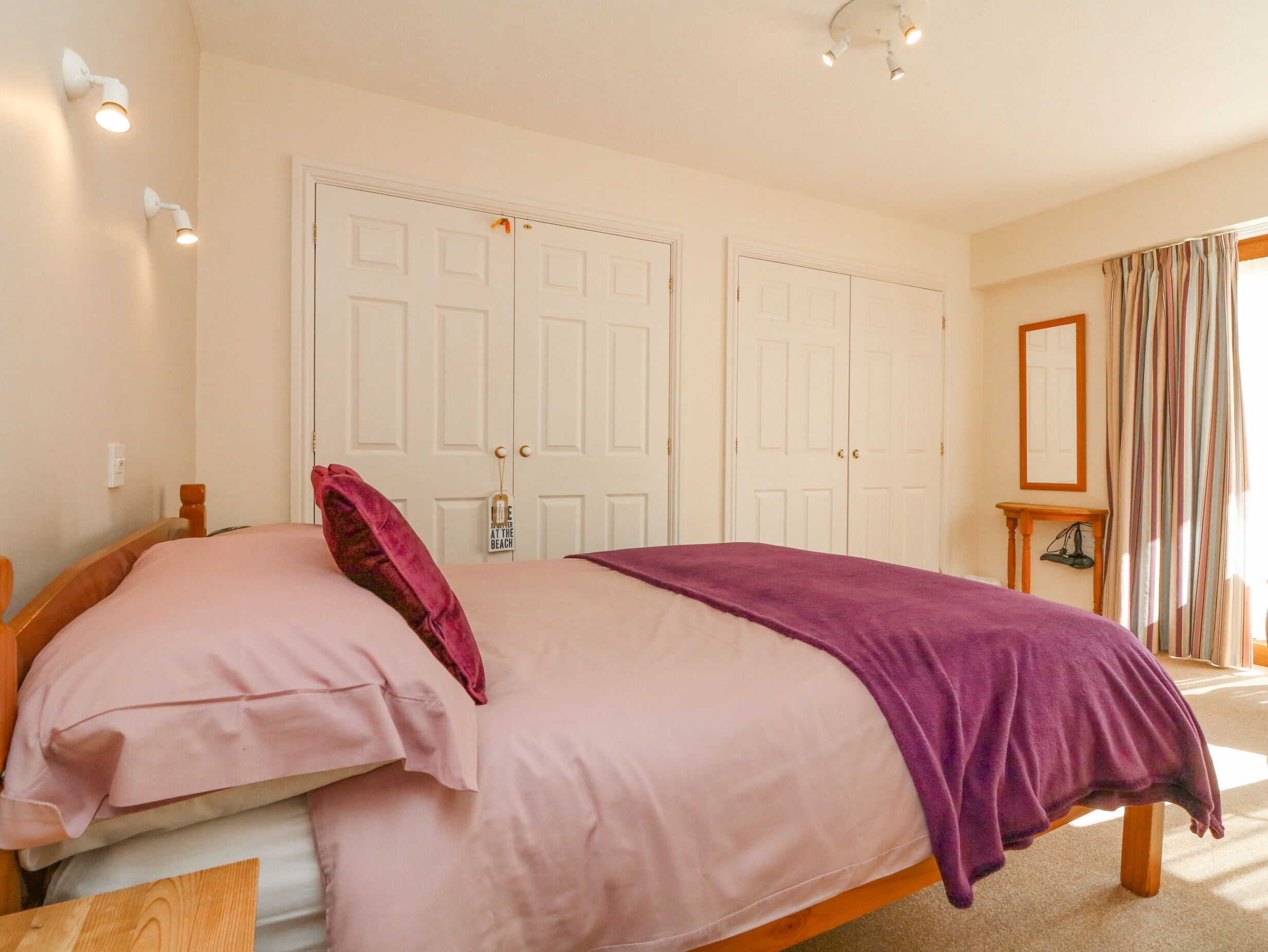 A bedroom with a bed, two doors, a nightstand, a mirror, and a window with curtains.
