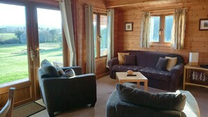 A cozy cabin interior with a sofa, armchair, and a small table. - Pennylands Hill View Lodge (Broadway)