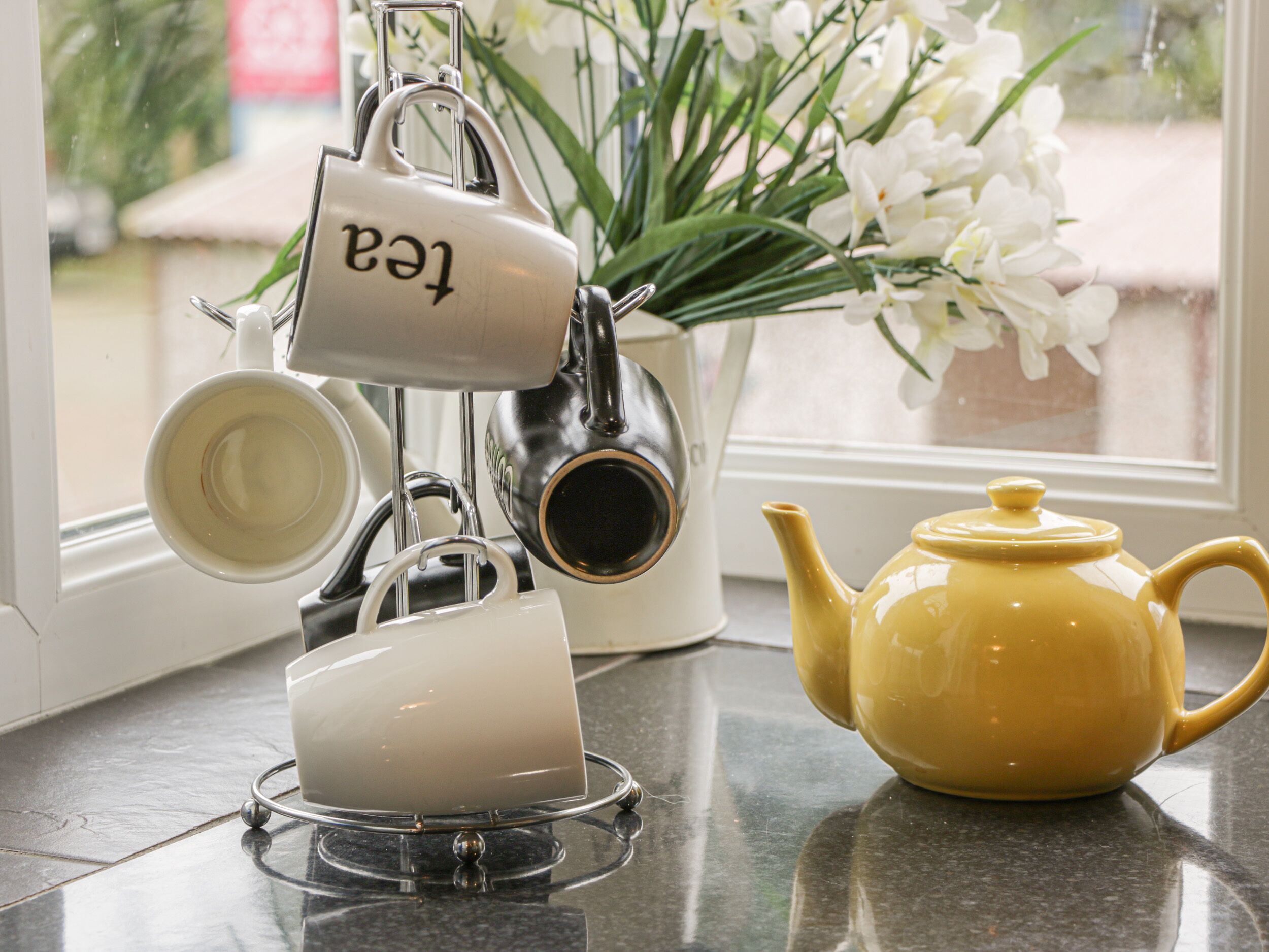 A kitchen counter with a tea kettle, a teapot, and a mug rack.