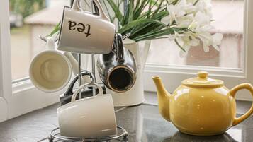 A kitchen counter with a tea kettle, a teapot, and a mug rack.
