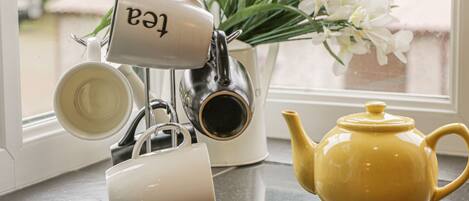 A kitchen counter with a tea kettle, a teapot, and a mug rack.
