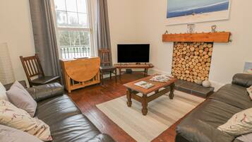 A living room with a sofa, a coffee table, a TV, and a fireplace with logs.