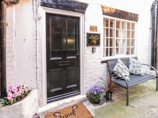A white building with a black door, a bench with patterned cushions, and a sign reading "Black Com Cottage". - Black Gem Cottage (Whitby)