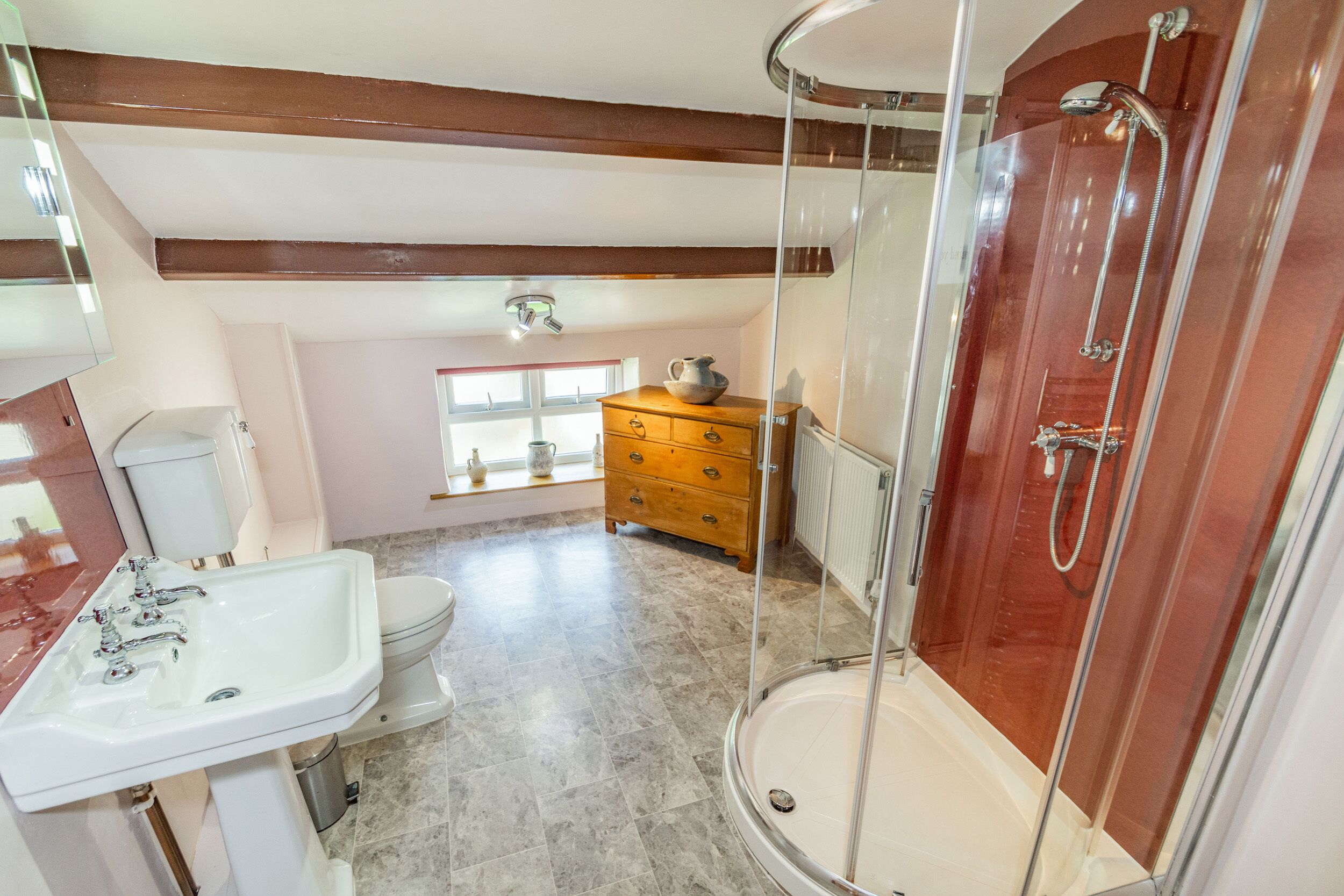 Un bagno con doccia vetrata, lavandino, WC e comò in legno.
