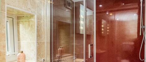 Un baño moderno con ducha envuelta en vidrio, lavamanos pedestal y pared revestida de mármol.