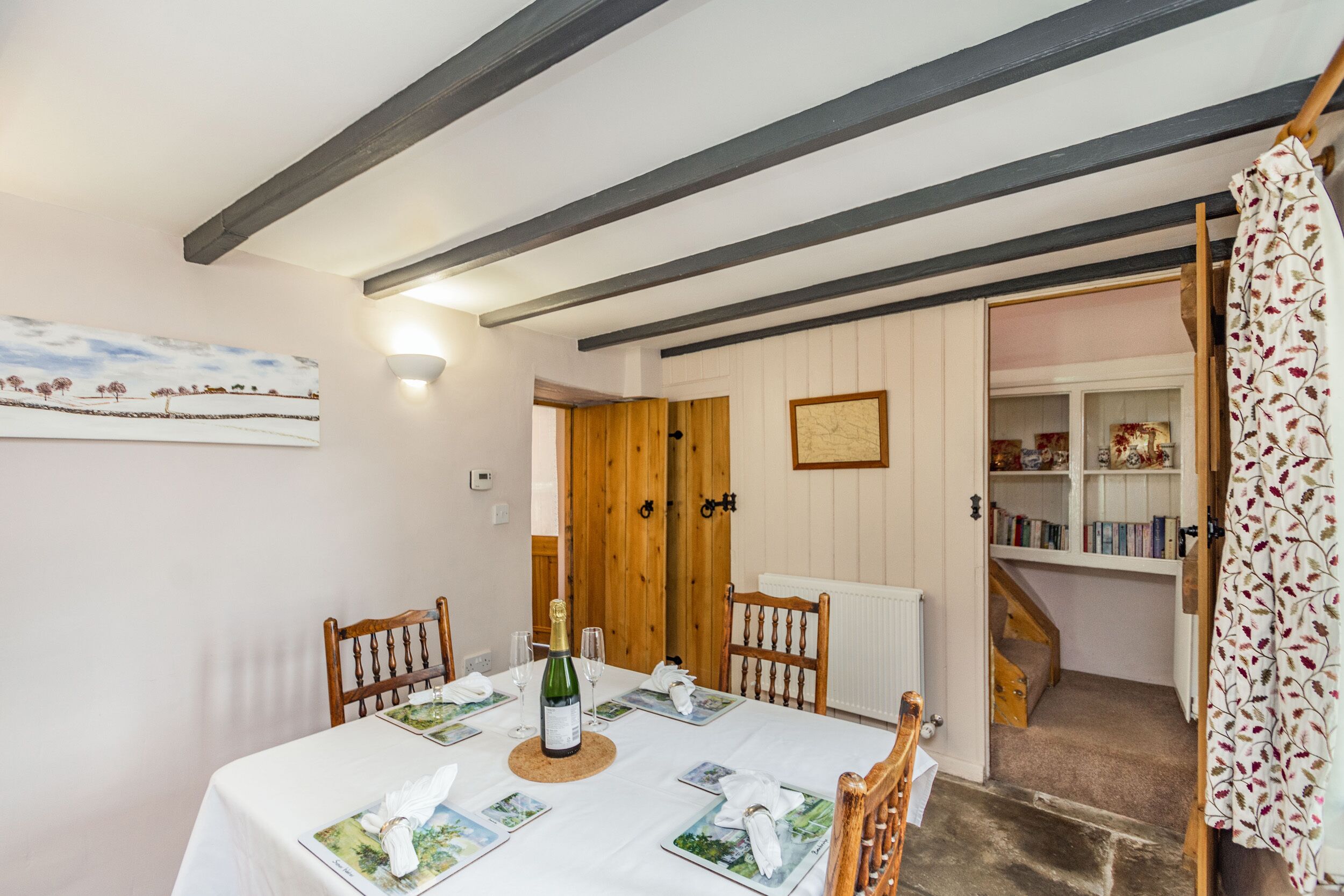 A dining area with a table set for four, wooden chairs, a bottle of champagne, and a framed landscape painting on the wall.