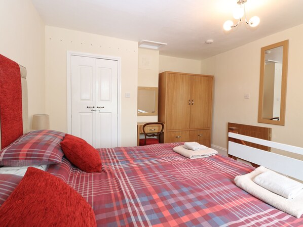 A bedroom with a bed, a wardrobe, a mirror, and a door. - 2 Lock Cottages (North Walsham)