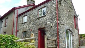 A stone building with a red door and windows, a wooden fence, and a paved entrance. - Crud-y-barcud (Llanwrda)