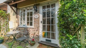 A cottage with a stone facade, a wooden porch, and a small patio with a table and chairs. - Old Town Cottage (Ludlow)
