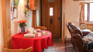 Un coin repas avec une table rouge dressée pour quatre personnes, une porte en bois portant un panneau indiquant la sortie de secours, et un canapé en cuir marron.