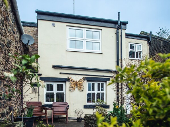 A two-story building with a satellite dish, a butterfly decoration, and a bench in the garden area. - Bastle House (Haltwhistle)