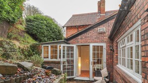 A brick house with a small garden area, a stone wall, and a paved path. - Beechlands Cottage (Frodsham)