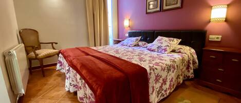 A bedroom with a bed, a chair, a radiator, and a nightstand.