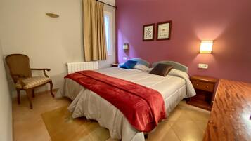 A bedroom with a bed, a chair, a nightstand, a lamp, and a window with curtains.