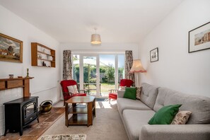 A living room with a sofa, chairs, a table, a fireplace, and a view through glass doors to an outdoor area. - 38 Dale End (King's Lynn)