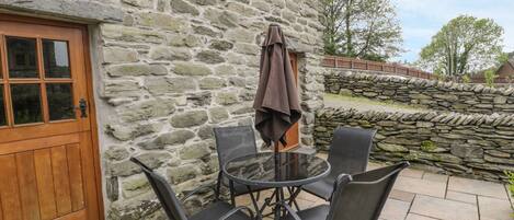 Un edificio de piedra con puerta de madera y un patio con una mesa redonda y cuatro sillas.