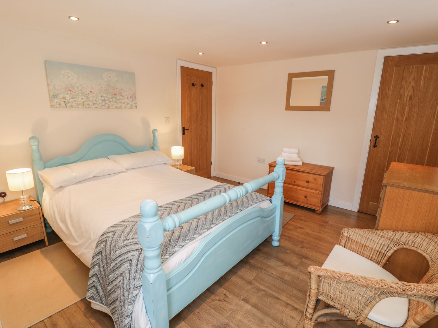 A bedroom with a bed, bedside tables, a nightstand, a chair, a wooden wardrobe, a mirror, and a painting on the wall.