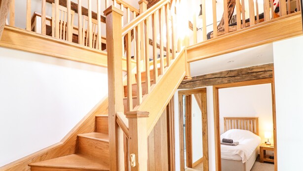 A wooden staircase leading to a bedroom with a bed and nightstand.