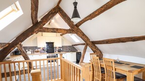 A loft-style kitchen with wooden beams, a dining area with wooden furniture, and a view of the kitchen through a skylight.