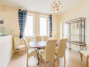 Enjoy meals in this dining area with a round table and six chairs, offering a view of the outside through a large window.