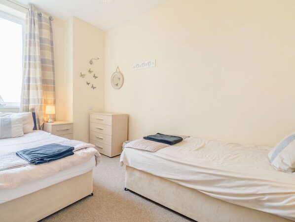 A bedroom with two beds, a dresser, a lamp, and butterfly wall decor. - Cairns Vista (Whitby)