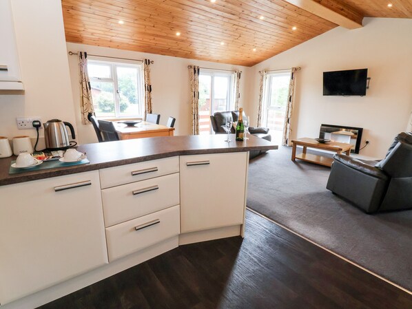 A modern kitchen with a wooden ceiling, a dining area with a table and chairs, and a living area with a sofa and a TV. - Callow Lodge 5 (Shrewsbury)