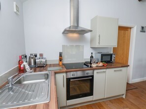 A compact kitchen with a sink, toaster, kettle, oven, microwave, and a cabinet.