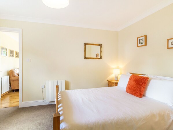 A bedroom with a large bed, a nightstand with a lamp, a radiator, and a mirror on the wall. - Norbank Garden Studio (Diss)