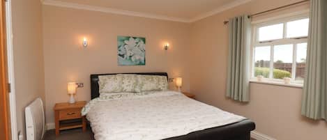 Un dormitorio con una cama grande, dos lámparas de noche, un radiador, una ventana con cortinas y una obra de arte colgada en la pared.