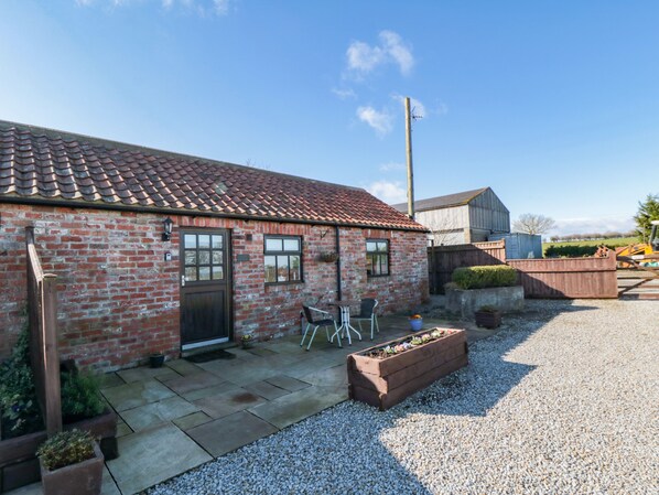 A brick building with a tiled roof, a door, and windows. There is a gravel area with a planter box and a chair outside. - Blakey (Saltburn-by-the-Sea)
