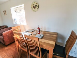 A wooden dining table with four chairs, a wine glass, a bottle of red wine, and a clock with a rooster design on the wall. - Blakey (Saltburn-by-the-Sea)