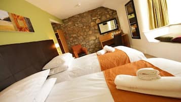 A hotel room with two beds, a stone wall, a television, and a window with curtains.