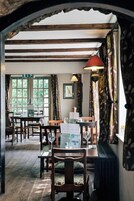 Un área de comedor con mesas y sillas de madera, un atril para el menú y una ventana con cortinas.