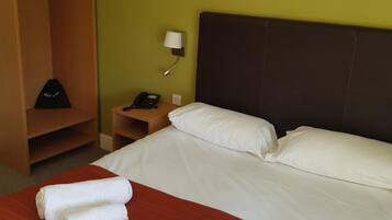 Une chambre d’hôtel avec un lit, deux serviettes enroulées, une armoire, une table de chevet avec une lampe et un tableau au mur.