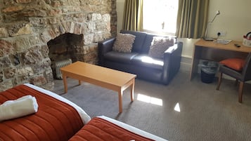 A cozy room with a stone fireplace, a sofa, a wooden table, and a bed with orange bedding.