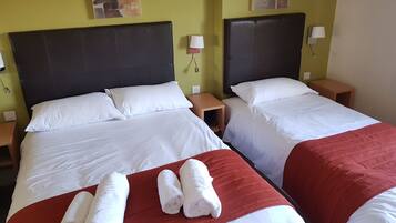 A hotel room with two beds, each with white linens and red bedspreads. There are two nightstands with lamps and a wall-mounted light.