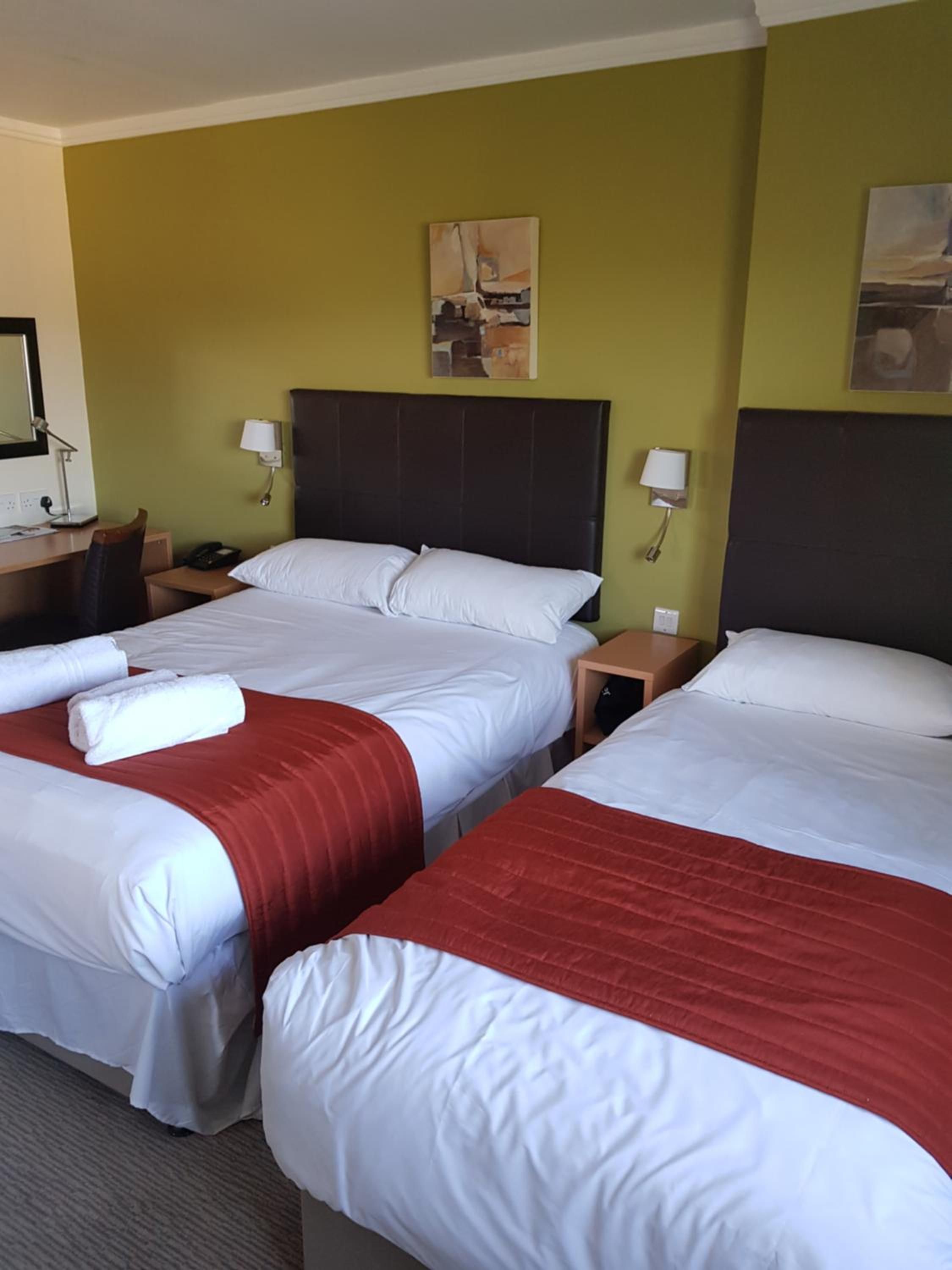 A hotel room with two beds, a desk, a chair, and a nightstand.