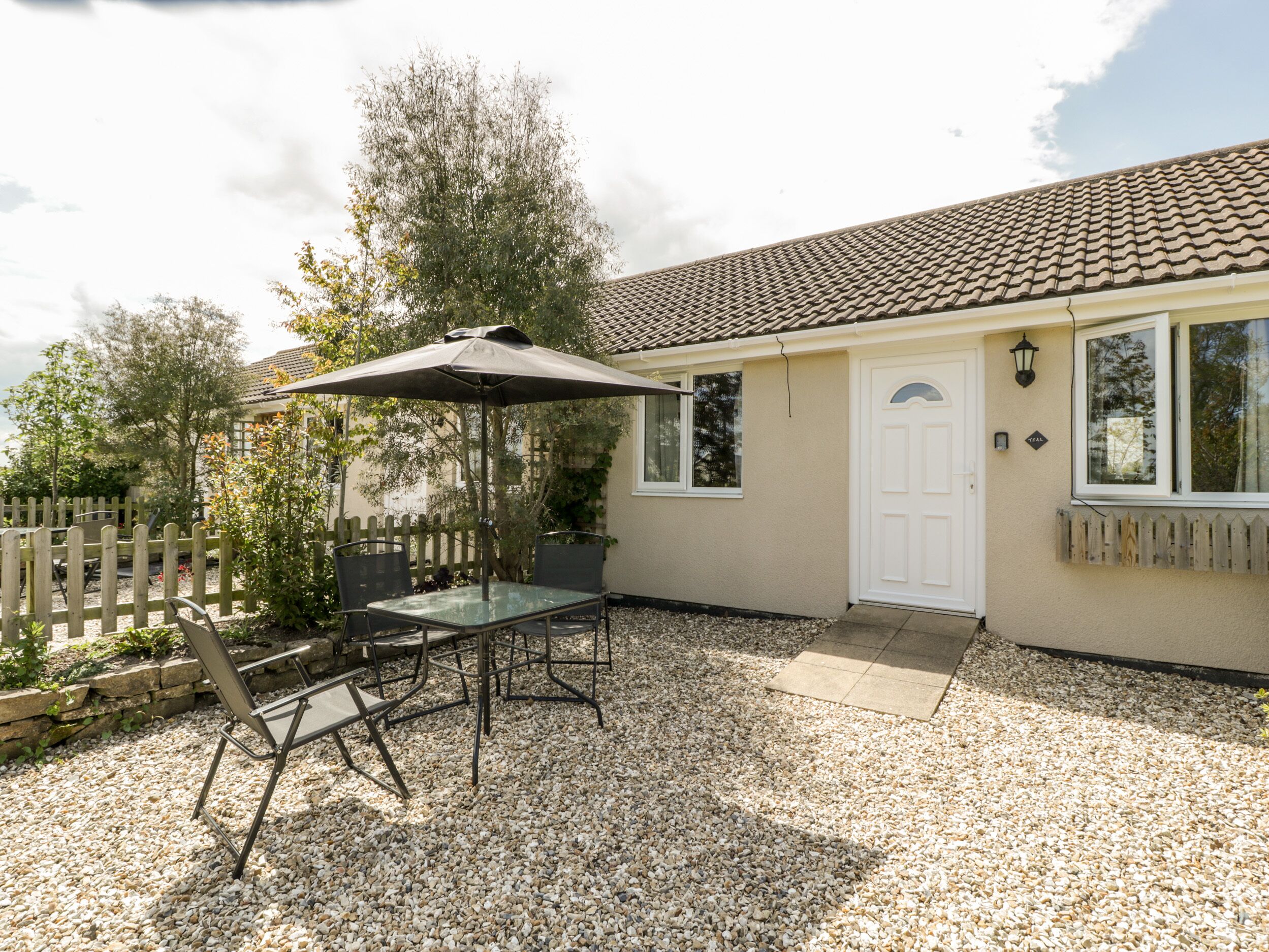 A patio with a table and chairs, a wooden fence, and a house with a tiled roof and a white door.