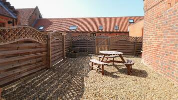 A courtyard with a wooden table and benches, surrounded by brick walls and a wooden fence.