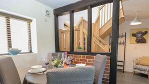 A dining area with a brick wall, wooden staircase, and a view of the upper floor. - Tricker's Cottage (Norwich)