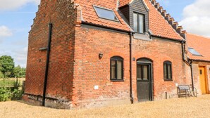 A red brick building with a sloped roof, a small window, and a door. - Tricker's Cottage (Norwich)