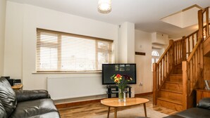 A living room with a wooden staircase, leather sofas, a TV, and a flower vase. - Muskoka Lodge (Radstock)